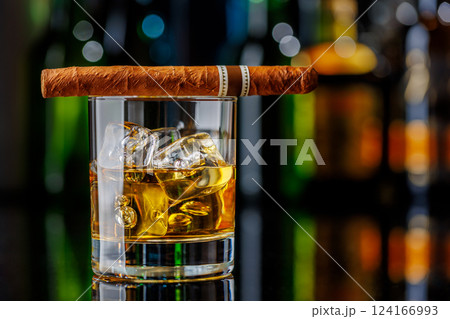 Whiskey on the rocks beside a lit cigar on a bar table 124166993
