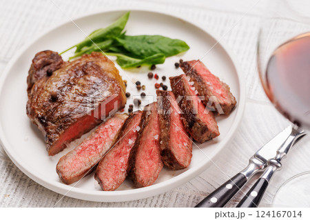 A perfectly cooked sliced striploin steak with a juicy, tender texture, served alongside a glass of rich red wine 124167014