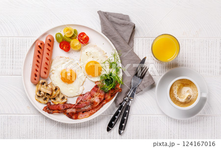 A classic breakfast plate featuring sunny-side-up eggs, crispy bacon, sausages, and fresh tomatoes 124167016