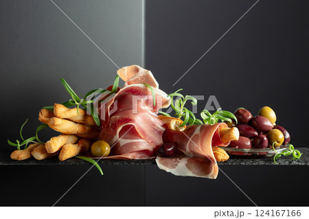 Prosciutto with bread sticks, olives, and rosemary on a black background. Prosciutto with bread sticks, olives, and rosemary on a black background. 124167166