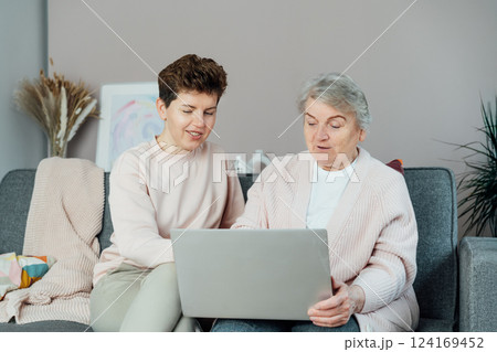 A young woman explaining her senior mother or grandma how to use laptop. Retired lady discovering technology for reading news, chatting with family, watching video, online consulting with doctor. 124169452