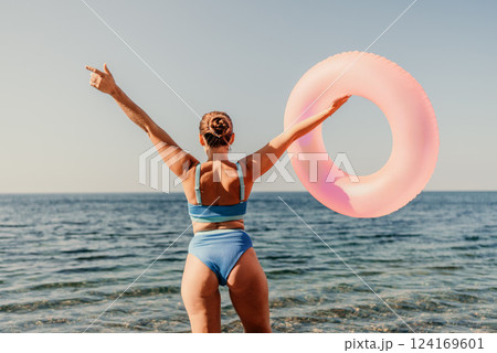 A woman is holding a pink inflatable ring in the ocean. Concept of fun and relaxation, as the woman is enjoying her time at the beach. 124169601