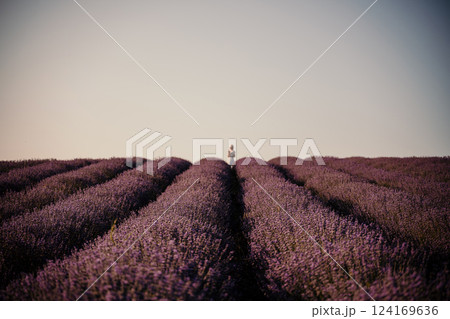 woman stands in a field of lavender. The sky is clear and the sun is shining brightly. The field is full of purple flowers, creating a peaceful and serene atmosphere. 124169636