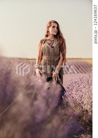 A woman is standing in a field of purple flowers, wearing a black dress and a black hat. 124169637