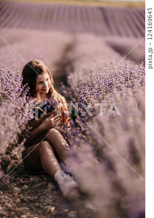 Girl is sitting in a field of purple flowers. She is holding a basket of flowers and smiling. Scene is peaceful and serene, as the girl is surrounded by the beauty of nature. 124169645
