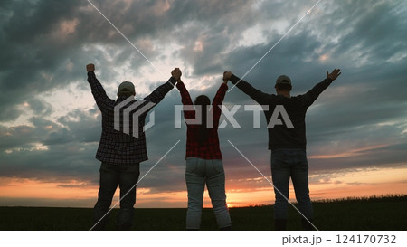 Farmer colleagues raising hands together at sunset field collaboration and teamwork concept back view. Man and woman agronomist agricultural workers celebrate success win victory triumph outdoor 124170732