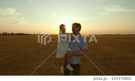 Father holding kid in arms in field at sunset. Happy cheery parent child kid strolling moving going across huge yellow meadow. Girl sits in man arms pointing with finger. Love fatherhood parenthood 124170802