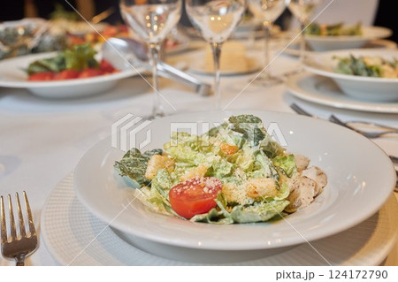 An elegant dinner setting with Caesar salad and fine dining essentials for a culinary experience 124172790