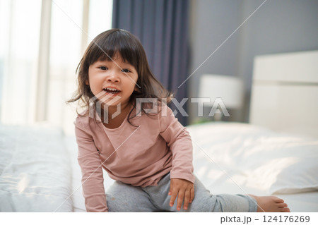 cheerful toddler girl playing and laughing on bed 124176269