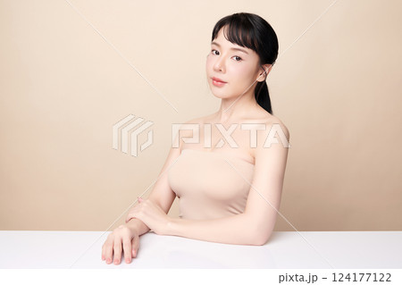 A beautiful young Asian woman with clean, fresh skin against a beige background. Skincare, facial treatment, cosmetology, beauty, and spa. An elegant portrait of an Asian woman. 124177122
