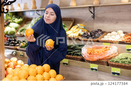 Girl in paranja making purchases in supermarket, choosing fresh oranges 124177384