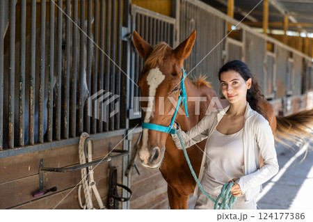Young woman leads horse out of stable 124177386