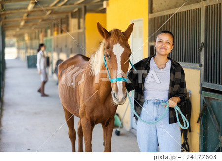 Young woman leading horse out of stable Young woman leading horse out of stable 124177603