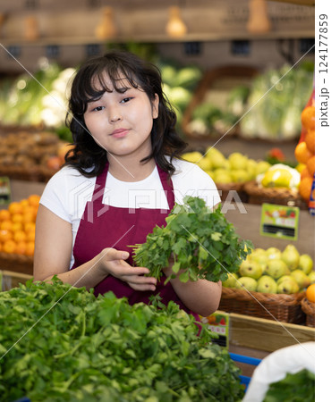Smiling young saleswoman holding bunch of cilantro in grocery store 124177859