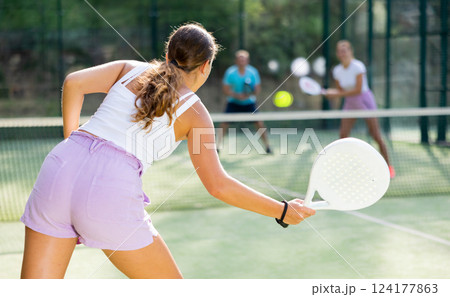 Sportive slim woman with racquet playing padel in court. View from back 124177863