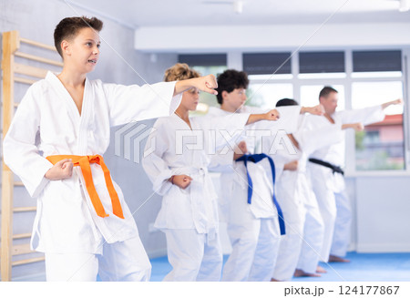 Teenager in kimono practicing punches during group martial arts workout 124177867