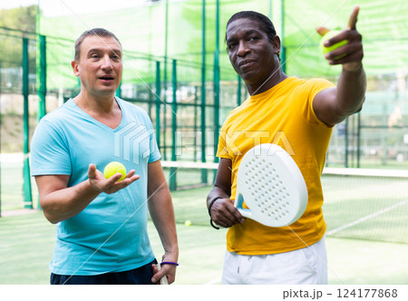 Two men padel tennis players on an outdoor court discussing something 124177868