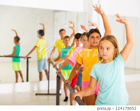 Focused tween girl practicing ballet positions near bar during group class Focused tween girl practicing ballet positions near bar during group class 124178052