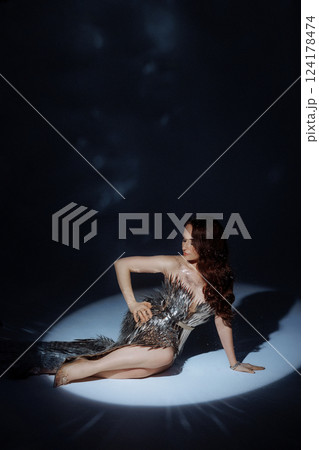 A woman in a metallic gown poses under a focused light. 124178474