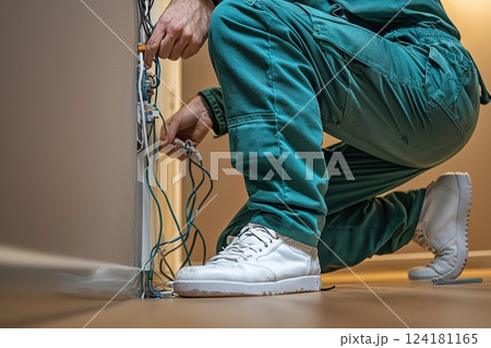 Electrician wearing green overalls repairing electrical wiring in a home interior 124181165