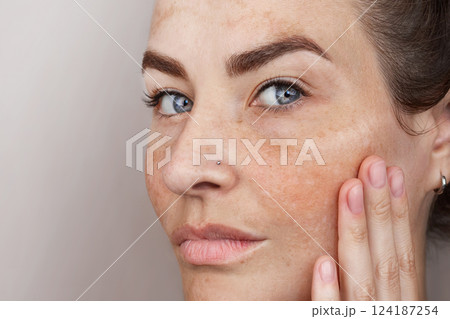 Close up caucasian woman's face with freckles or age spots. Age spots on the face. Woman with blue eyes looks at camera 124187254