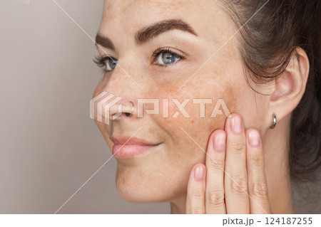 Portrait of cropped caucasian middle aged woman face with freckles touching skin by hand. Age spots on the face. Woman with blue eyes Portrait of cropped caucasian middle aged woman face with freckles touching skin by hand. Age spots on the face. Woman with blue eyes 124187255