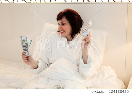 Woman with money in her hands dancing while lying in bed Woman with money in her hands dancing while lying in bed 124188420