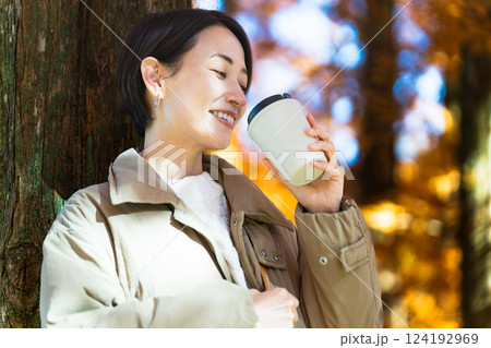 紅葉を楽しみながらホットドリンクを飲む女性　ライフスタイルイメージ 124192969
