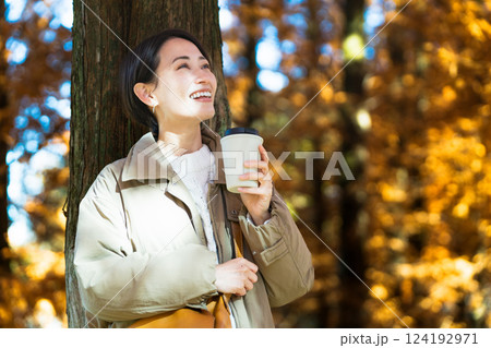 紅葉を楽しみながらホットドリンクを飲む女性　ライフスタイルイメージ 124192971