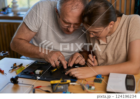 Grandfather and granddaughter work together on an electronics project 124196234