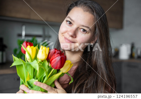Portrait of young woman with a bouquet of red and yellow tulips at home. Congratulations and a gift on International Women's Day or Mother's Day 124196557