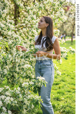 Young woman standing in the park near a pear tree that has blossomed with white flowers in the spring in Prague 124196564