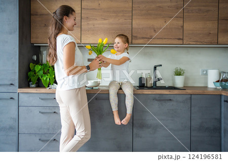 Little girl giving flowers to her mum on the home kitchen. Mothers day, birthday or International Women's Day 8 march concept 124196581