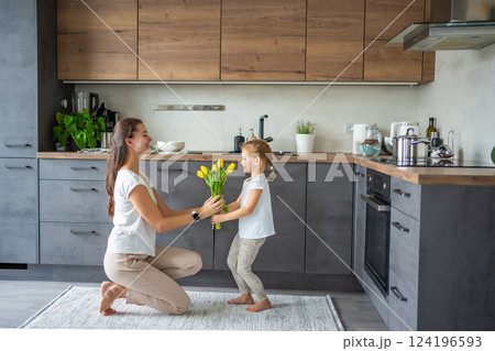 Little girl giving flowers to her mum, while woman cooking on the kitchen. Mothers day, birthday or International Women's Day 8 march concept Little girl giving flowers to her mum, while woman cooking on the kitchen. Mothers day, birthday or International Women's Day 8 march concept 124196593