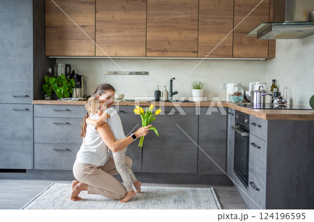 Little girl giving yellow tulips to her mum on the home kitchen. Mothers day, birthday or International Women's Day 8 march concept Little girl giving yellow tulips to her mum on the home kitchen. Mothers day, birthday or International Women's Day 8 march concept 124196595