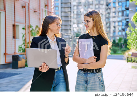 Female teacher talking to teenage student girl, outdoor, educational building background Female teacher talking to teenage student girl, outdoor, educational building background 124196644