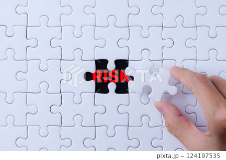 Risk Management and Identification Concept. A hand places a puzzle piece into a nearly complete puzzle, revealing the word Risk in red, process of identifying and managing risks within complex systems 124197535