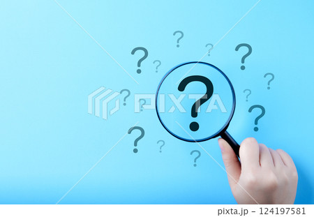 Question Mark and Root Cause Analysis Concept. A hand holding a magnifying glass over a large question mark surrounded by smaller ones on a blue background, symbolizing analysis and problem-solving. 124197581