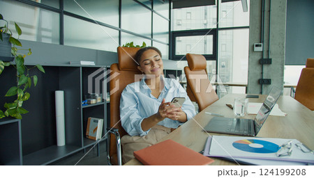 A young professional woman multitasking in a modern office, talking on the phone while analyzing documents at a desk with a laptop, plants, and stylish furniture A young professional woman multitasking in a modern office, talking on the phone while analyzing documents at a desk with a laptop, plants, and stylish furniture 124199208