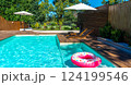Modern backyard swimming pool with turquoise water, wooden deck, umbrellas, lounge chairs, and pink donut inflatable 124199546