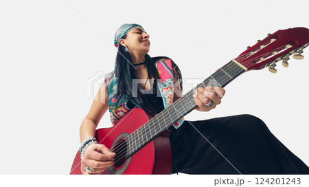 Joyful female guitarist in traditional-inspired outfit smiling while playing, enjoying musical flow and creative freedom Joyful female guitarist in traditional-inspired outfit smiling while playing, enjoying musical flow and creative freedom 124201243