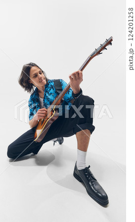 Young energetic man in tropical shirt, sitting and passionately playing electric guitar against white background. Young energetic man in tropical shirt, sitting and passionately playing electric guitar against white background. 124201258