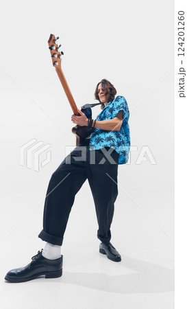 Low angle view of stylish young man in tropical shirt, energetically playing electric guitar against white background 124201260