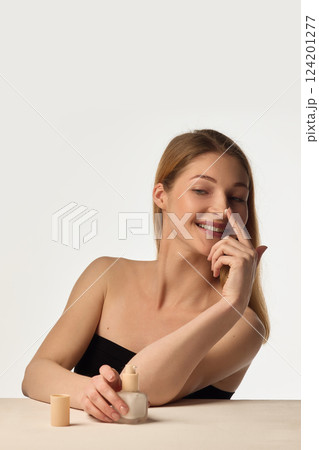 Joyful skincare ritual. Young woman applying nourishing cream to her nose with playful smile against white background 124201277