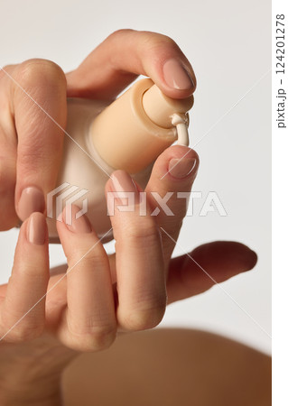 Luxury skincare product close-up. Hands pressing pump bottle with hydrating cream for smooth application. 124201278
