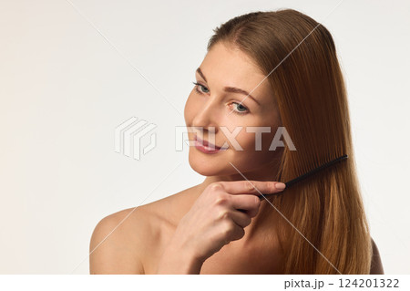 Young woman brushing long silky hair, emphasizing healthy hair care and beauty against white background. 124201322