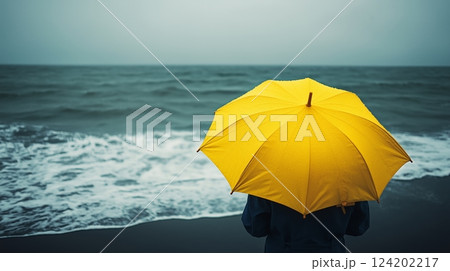 Bright yellow umbrella against stormy ocean backdrop 124202217