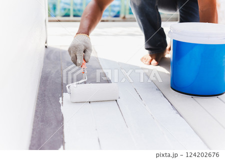 Worker painting decking floor in white color with a roller. Worker painting decking floor in white color with a roller. 124202676