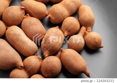 Ripe whole tamarind fruits on black ceramic. Unshelled pods. Tropical sweet vegan snack. Exotic dessert.  124203231