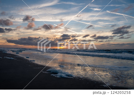 A stunning sunset over the ocean with cloud trails and gentle waves creates a picturesque scene A stunning sunset over the ocean with cloud trails and gentle waves creates a picturesque scene 124203258